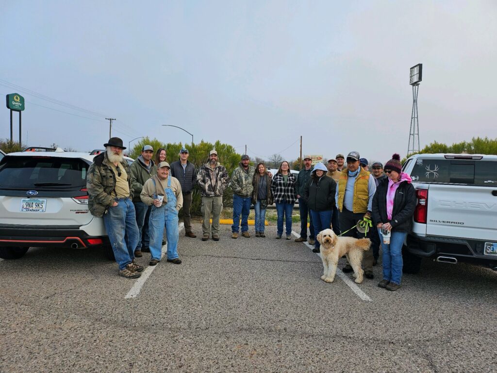 A group of people with a dog standing in a parking lot in Southern Arizona, possibly preparing for an outdoor activity or gathering related to Water Catchment Restoration.